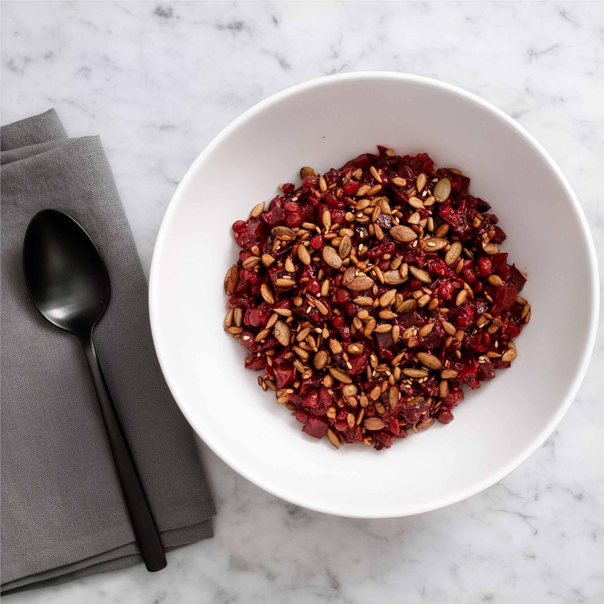 Airheads beetroot, lentil, and seed salad in a ceramic bowl, on a marble surface with a spoon and napkin.