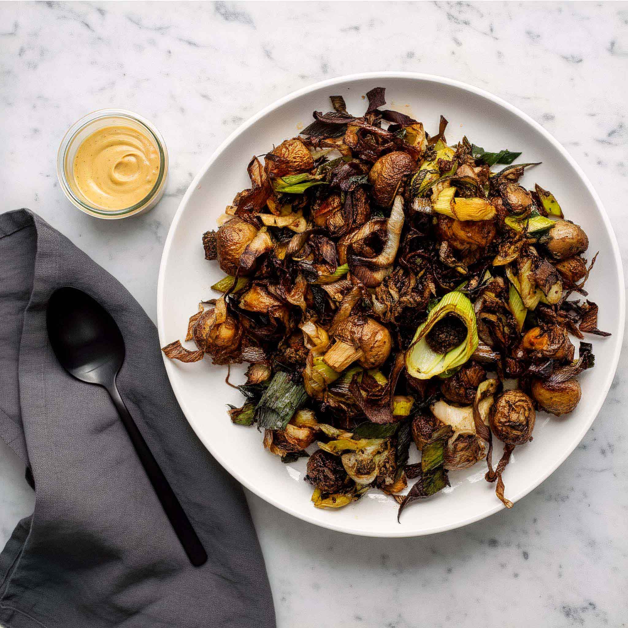 White plate of Airheads buttered leeks and mushrooms and a small bowl of mustard on a marble surface.