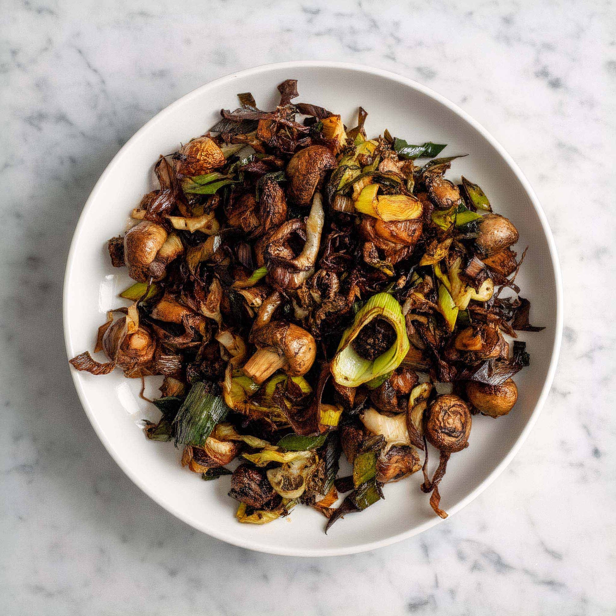 White plate with air fried leeks and mushrooms in garlic butter sauce on a marble background.