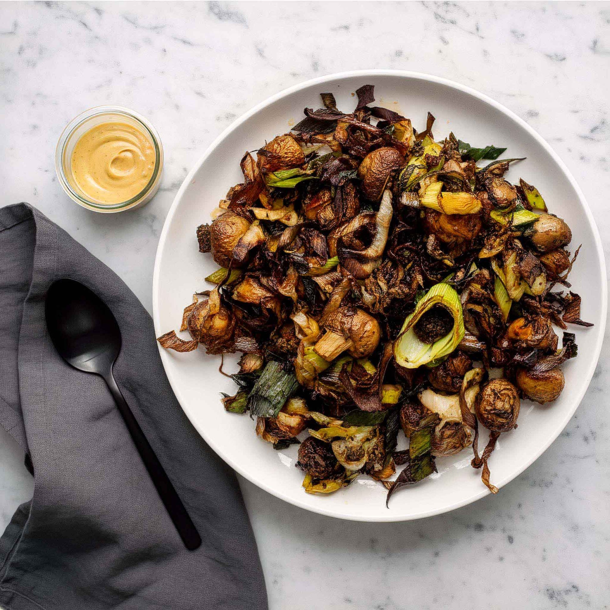 White plate of Airheads buttered leeks and mushrooms and a small bowl of mustard on a marble surface.