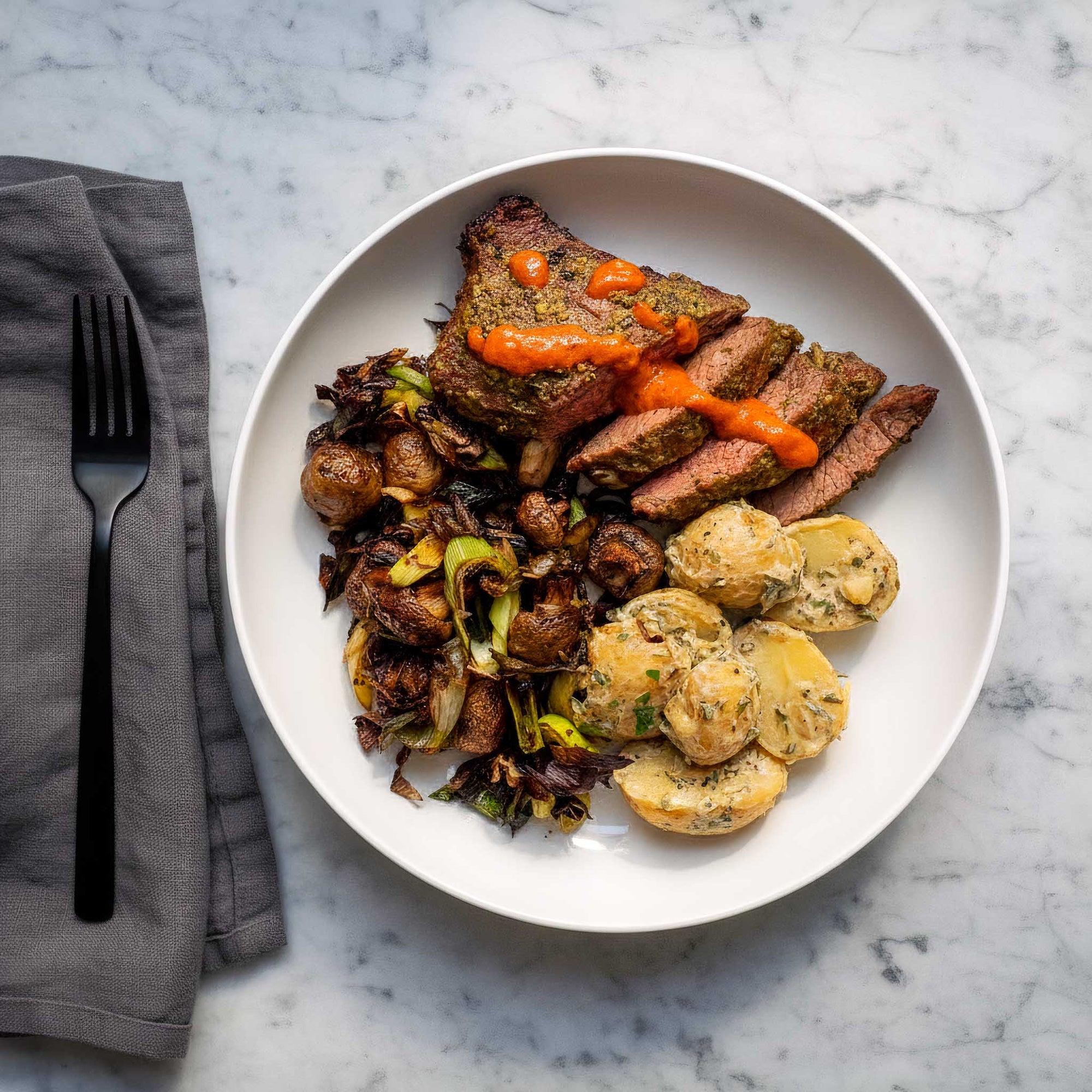 Plated dish buttered leeks and mushrooms served with chimichurri flank steak and dijon mustard potato salad on a marble surface.