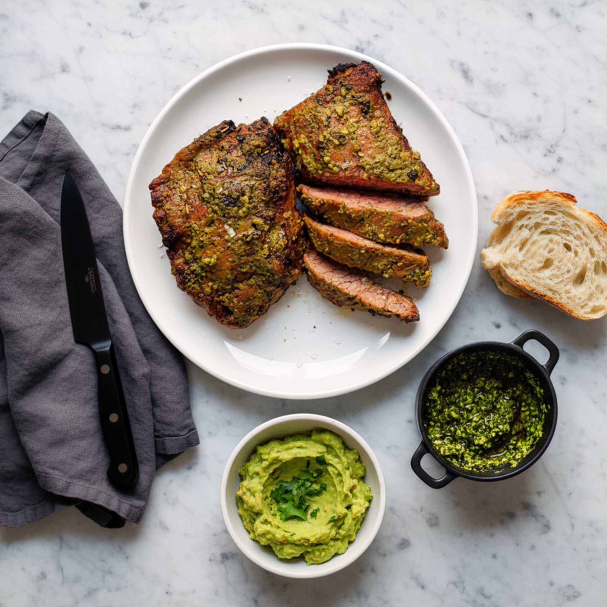 Plated dish of Airheads chimichurri flank steak served with herb sauce, smashed avocado and bread on a marble surface.