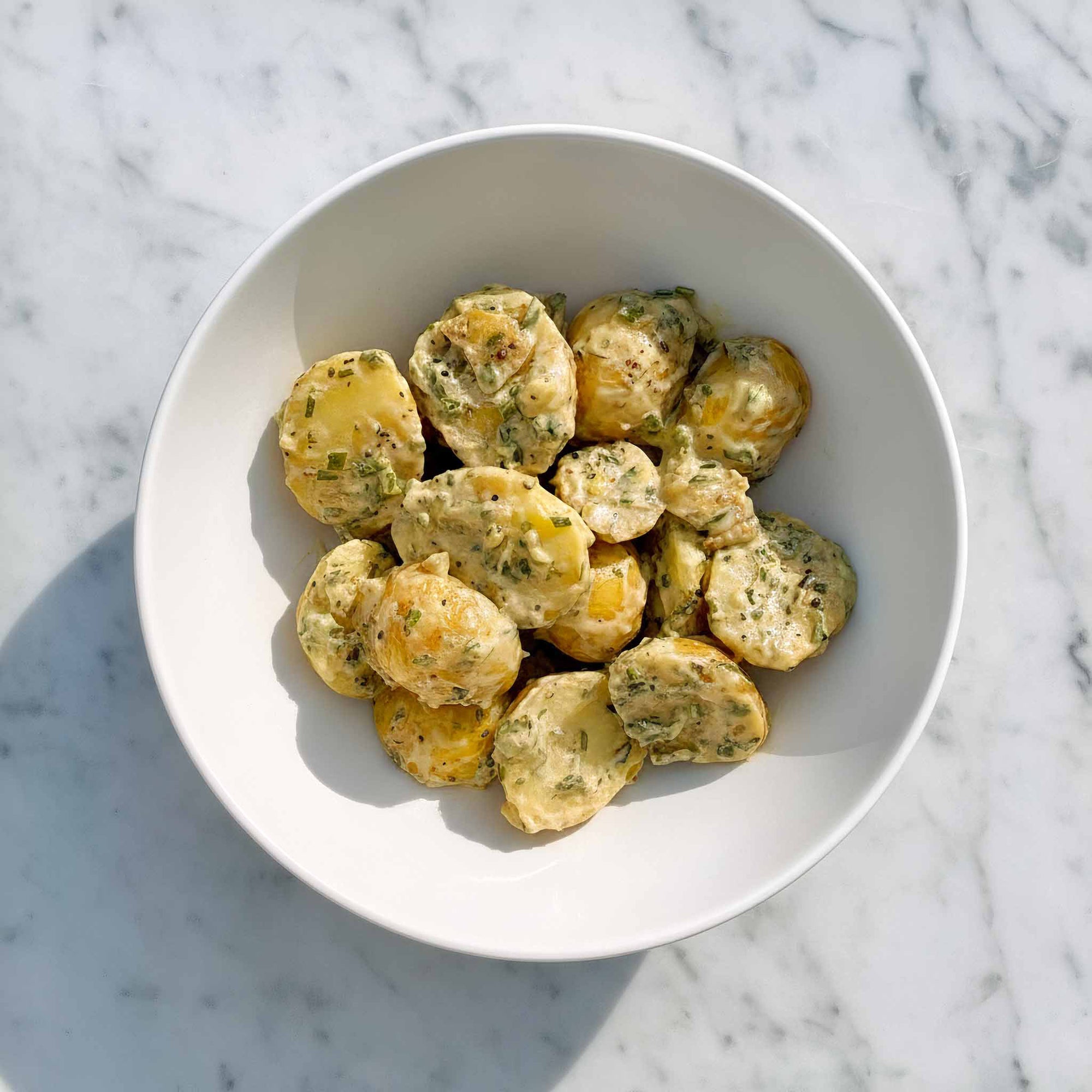 White bowl with dijon mustard potato salad on a marble surface.