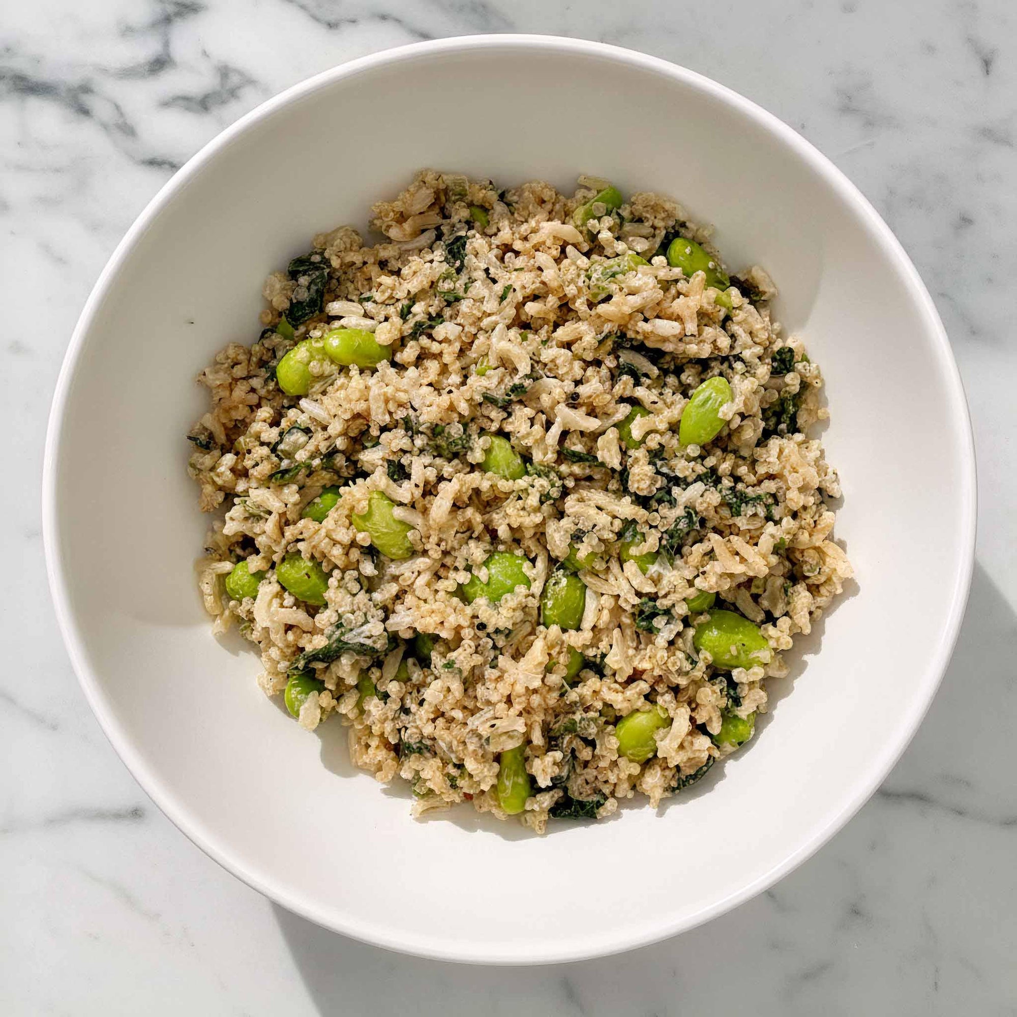 White bowl with edamame quinoa and brown rice salad in a white ceramic bowl on a marble surface.