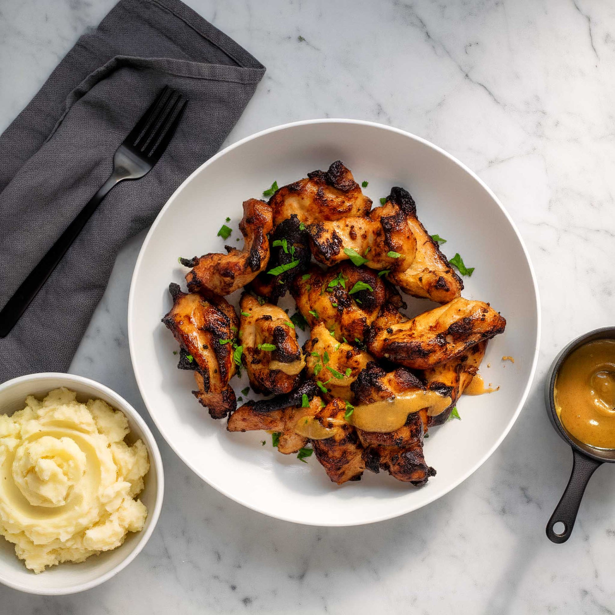 Plated honey mustard chicken thighs with a side of mashed potatoes and a dipping pot of honey mustard sauce on a marble surface.