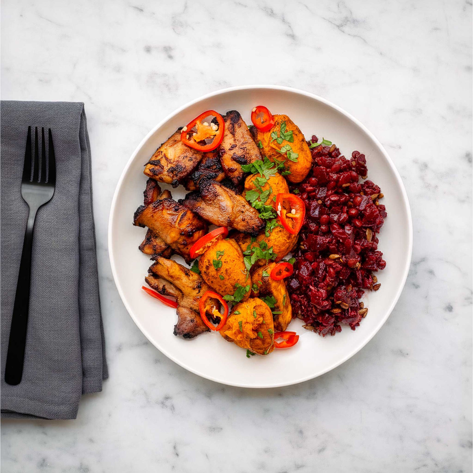 Plated dish of honey sesame chicken thighs with roasted hot shake seasoned sweet potato and a beetroot lentil salad, on a marble surface.
