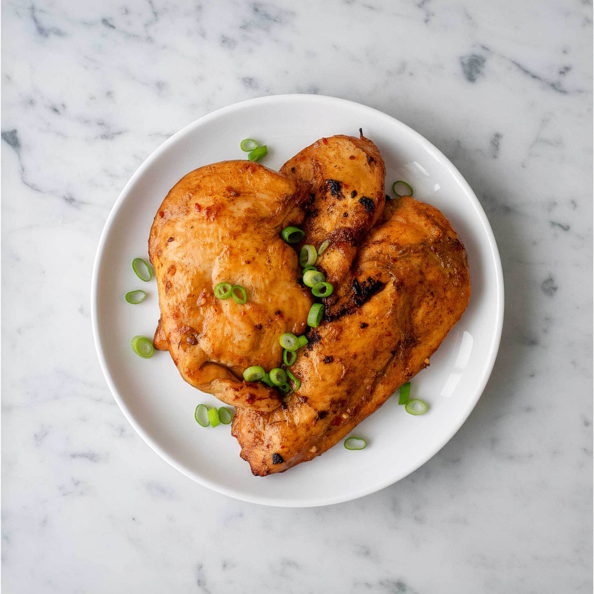 Korean BBQ chicken breast  dish on a white plate with green spring onions, set against a marble background.