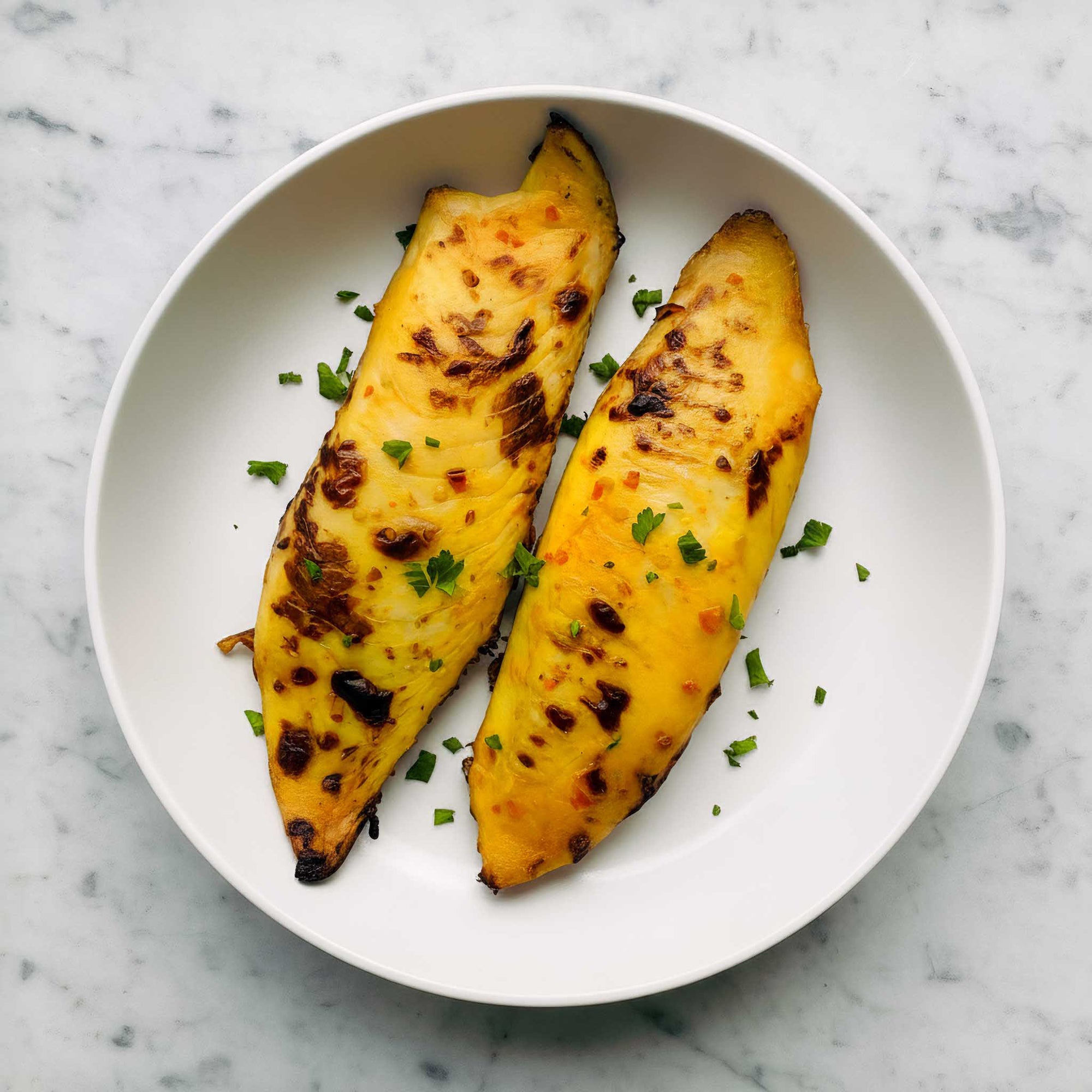 Two air fried mango-glazed tilapia fillets  on a white plate with green herbs on a marble background.
