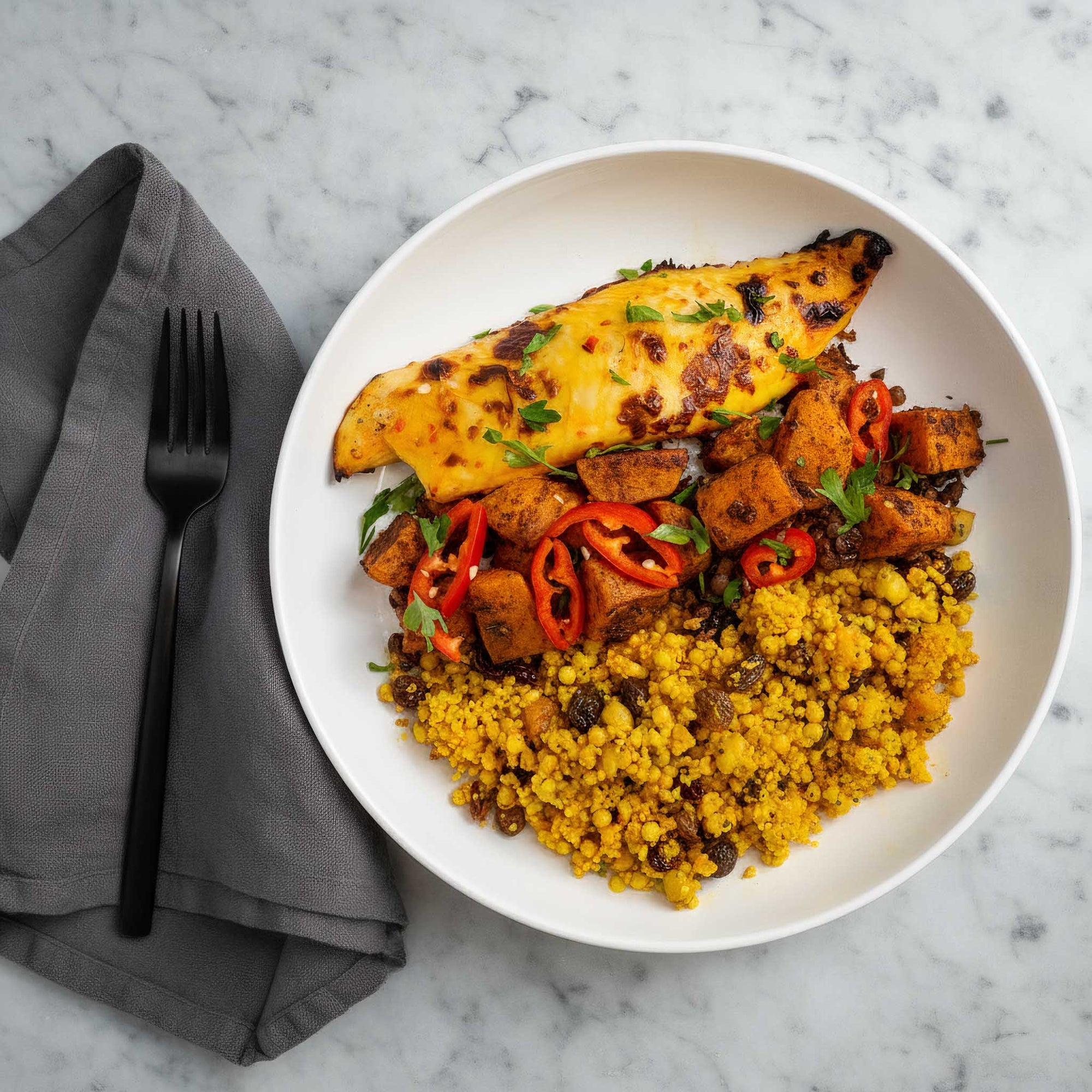Plated dish with mango tilapia fillets, spiced squash and chickpeas, and yellow couscous on a marble surface.
