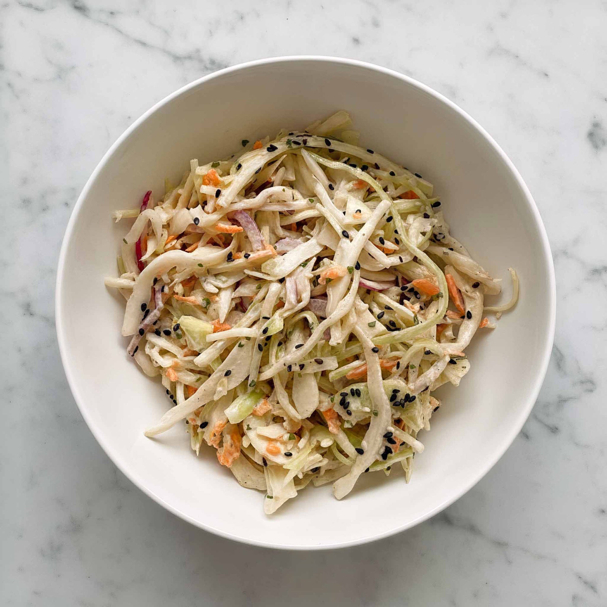 Maple mustard dressed coleslaw in a white bowl on a marble surface.