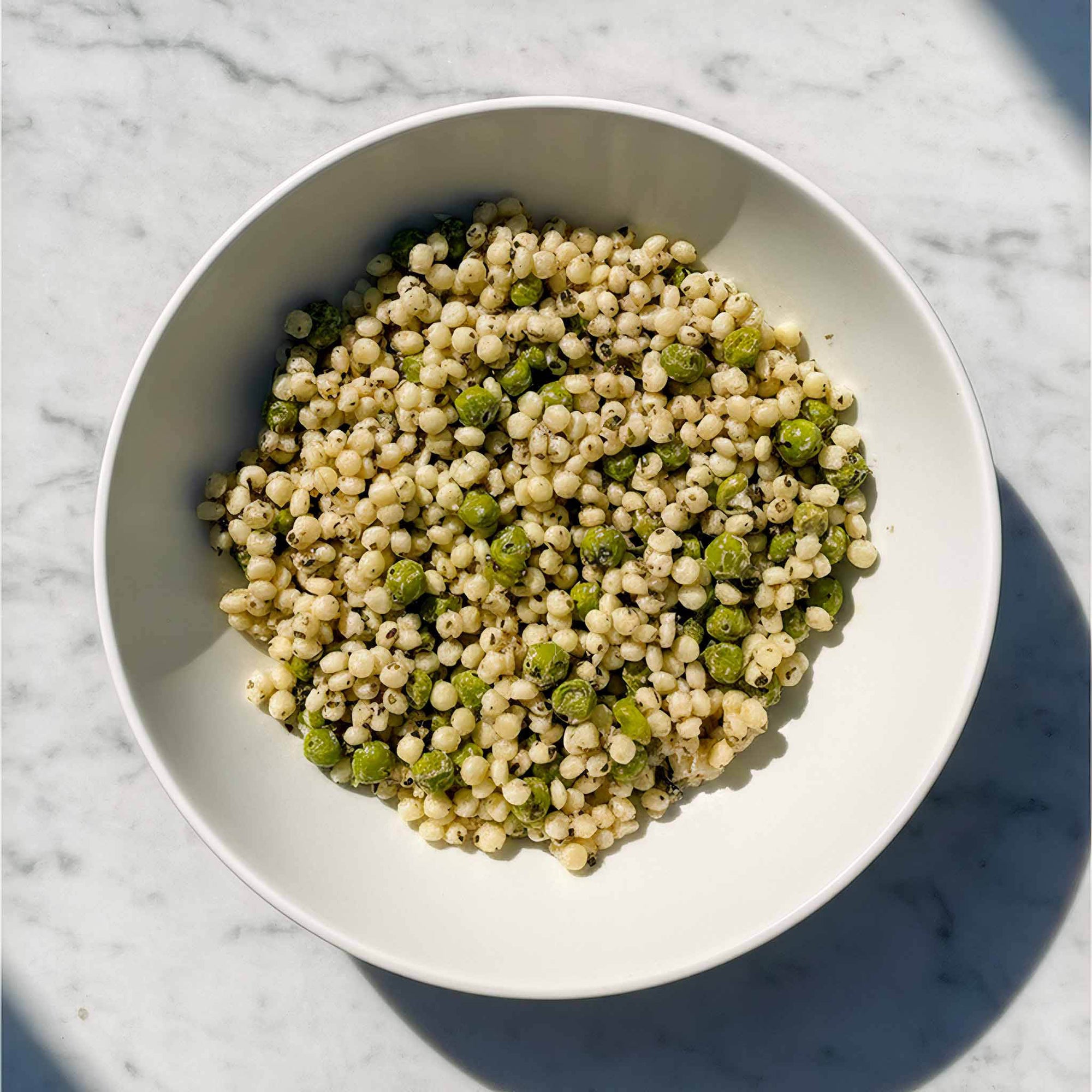 White bowl with giant minted couscous salad topped on a marble surface.