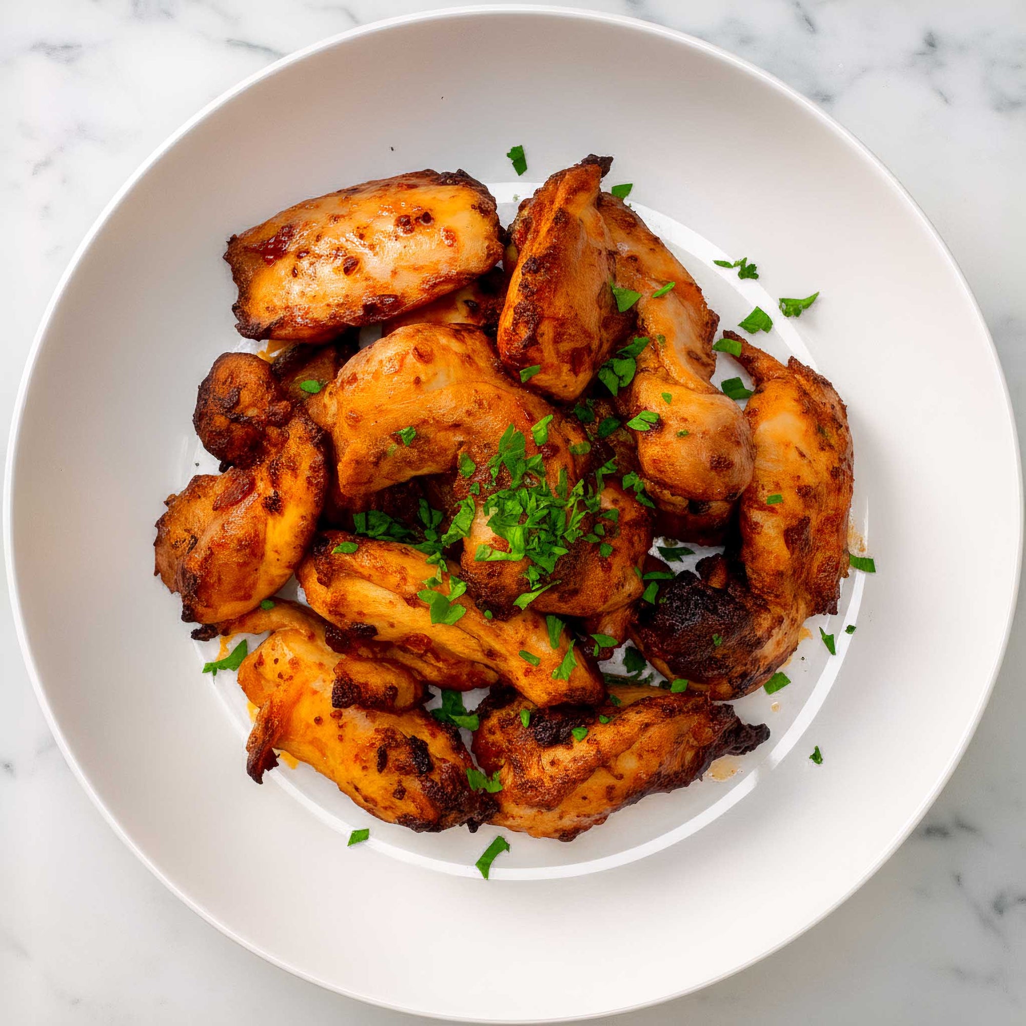 Close-up of air fried  peri peri chicken thighs seasoned with green herbs on a white plate.