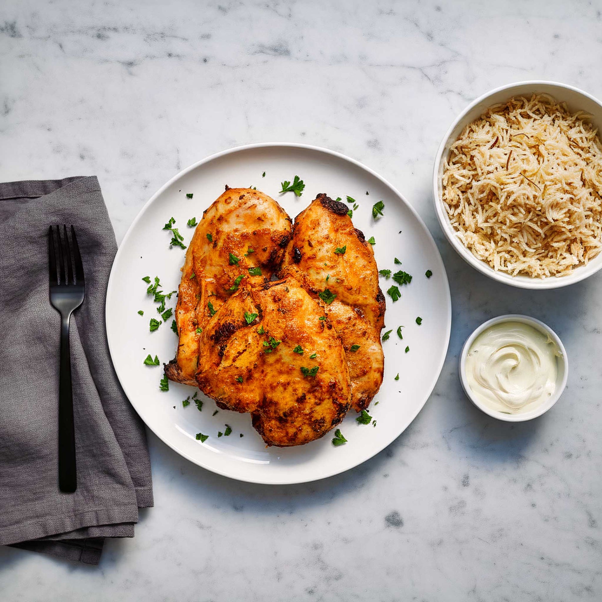 Plated dish of smokey harissa chicken breasts with a side of Persian rice and sauce on a marble surface.