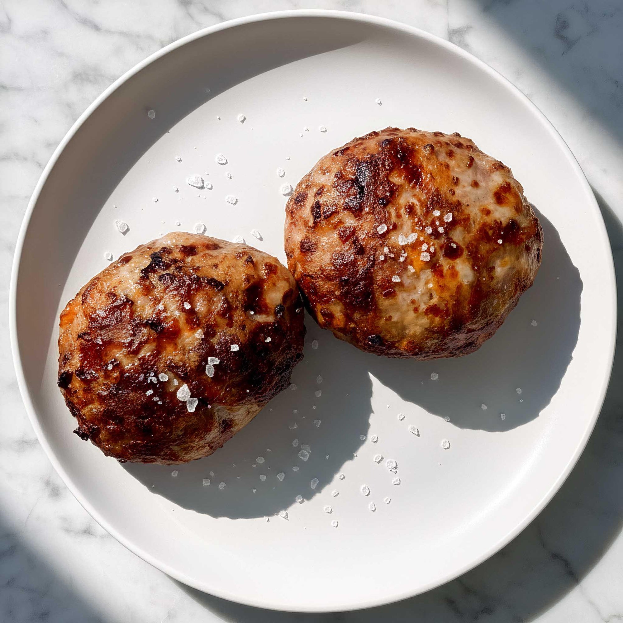 Two air fried smokey bacon and pork patties on a white plate with a marble background.