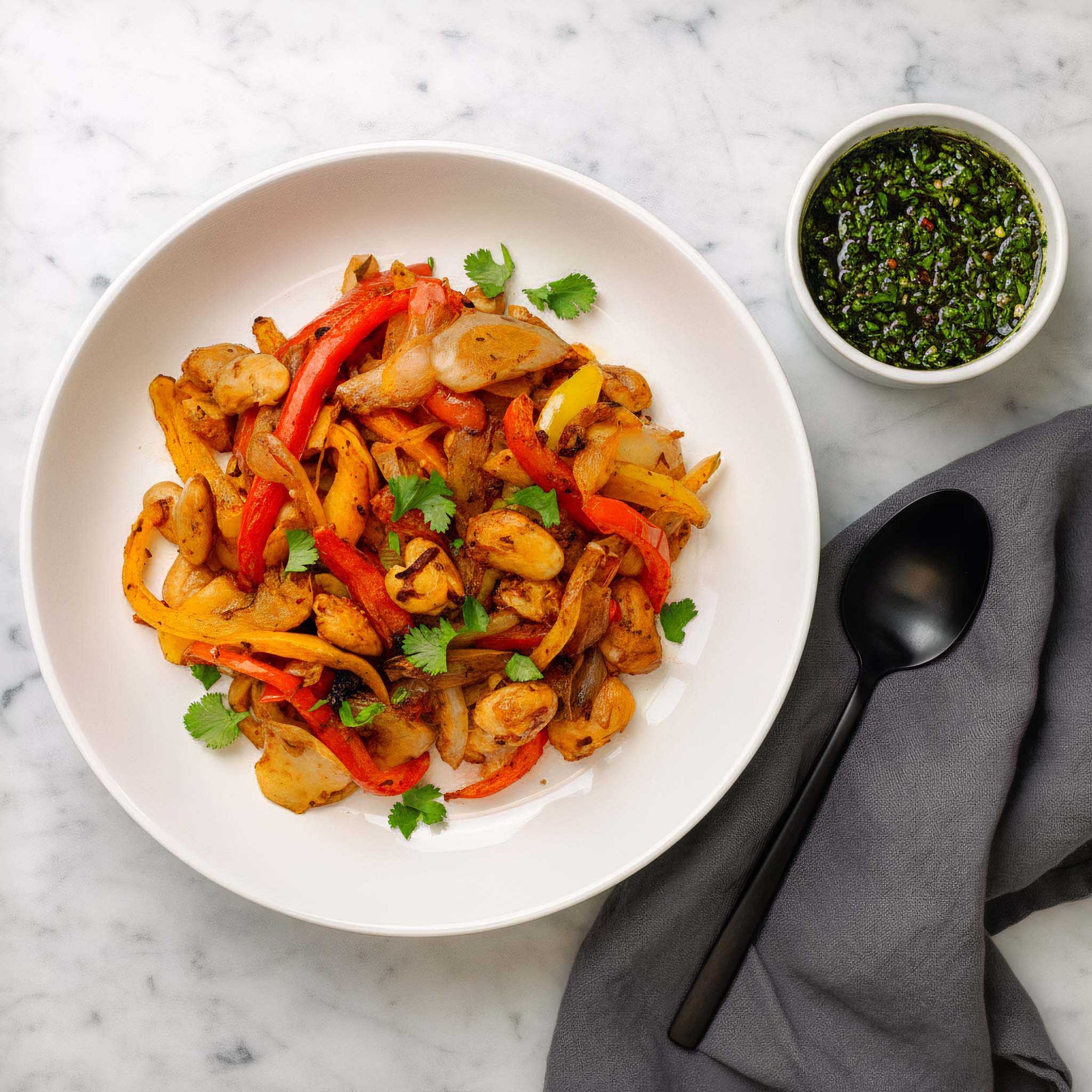 Airheads Tex-Mex peppers, onions and butter beans, alongside a pot of chimichurri sauce in a white bowl, on a marble surface.
